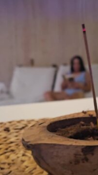 Incense smolders in the holder, and a woman is comfortably settled on a spa lounger, creating a cozy, relaxing atmosphere