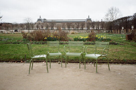 Green metal chairs scattered on a gravel path in a public park