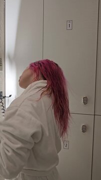 Blow drying pink hair in a bathroom with bright light