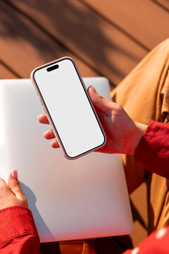 Woman holding phone mockup with blank screen over closed laptop
