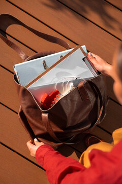 Woman packing work folders and headphones into leather tote