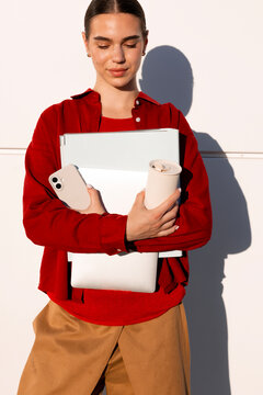 Woman holding work essentials beside a sunlit white wall