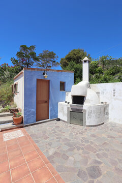 Blue cottage with outdoor stone oven on tiled patio
