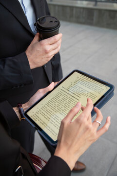 Businesswoman reading document on tablet while holding coffee