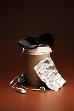 Black sunglasses on top of a coffee cup, earbuds and blister pack