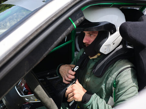 Rally driver fastening safety harness in racing car