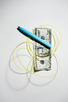 Twenty dollar bill with a tangled yellow wire around with a blue pen