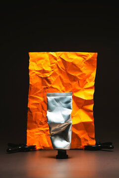 Squeezed metal cream tube in front of wrinkled orange backdrop