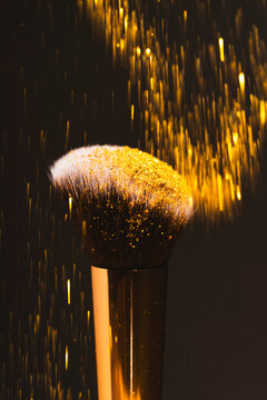 Closeup shot of makeup brush under gold glitter rain