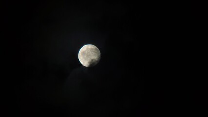 Bright full moon shining through thick dark gray clouds at night creates mysterious celestial atmosphere for astronomy projects and digital art backgrounds prints. © MatStudio