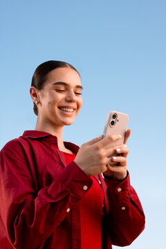 Smiling woman using smartphone against clear blue sky outdoors