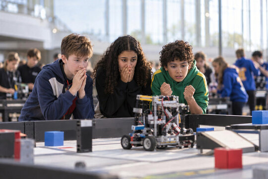 Excited teen students watching robot compete at school robotics competition in large hall, stem education event