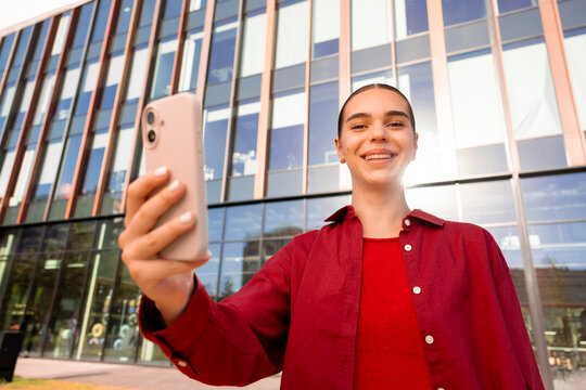 Smiling woman taking selfie outside contemporary office building
