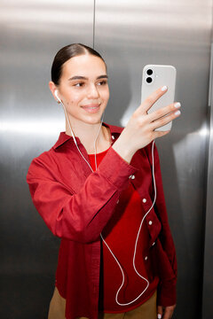 Woman enjoying mobile entertainment with earphones in elevator