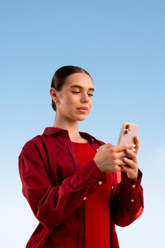 Woman texting on smartphone in red shirt under blue sky