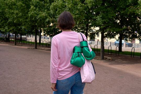 Woman walks in a park while carrying green boxing gloves and a bag