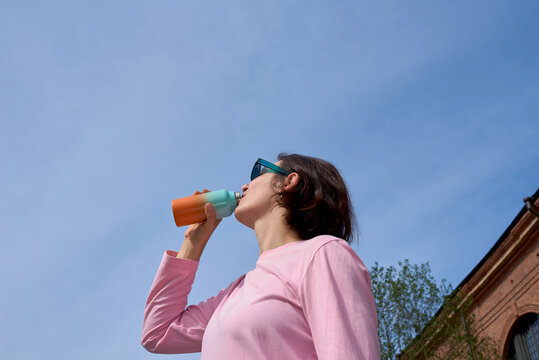 Woman drinking water from a colorful bottle under a blue sky