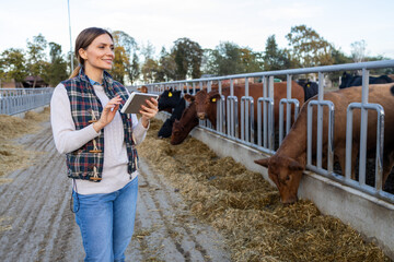 Young woman farmer using a digital tablet to monitor cattle in a modern outdoor livestock farm © SISMIZ