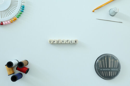 UPCYCLE spelled with letter tiles among thread, needles, pins and sewing tools on a clean flat lay with generous copy space.
