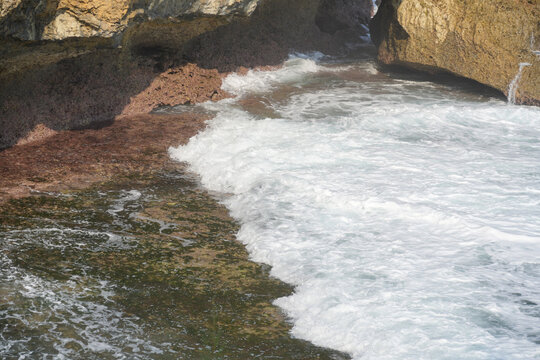 Ocean waves crashing against rocky tropical cliffs with white foam water.