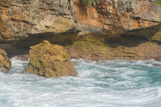 Ocean waves crashing against rocky tropical cliffs with white foam water.