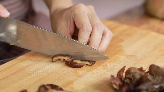 Chef slicing shiitake mushrooms on a wooden cutting board