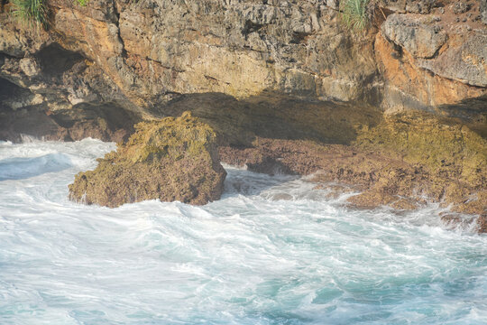Ocean waves crashing against rocky tropical cliffs with white foam water.