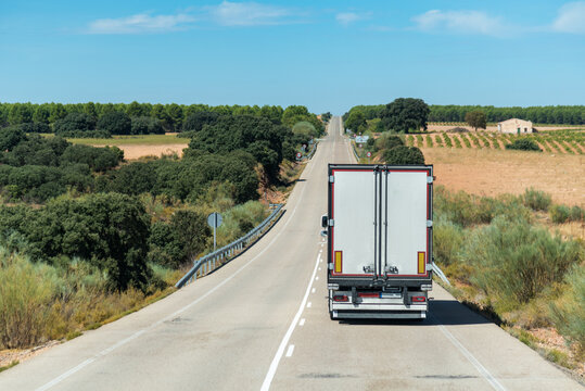 Refrigerated truck driving along a long straight road through farmland and forests