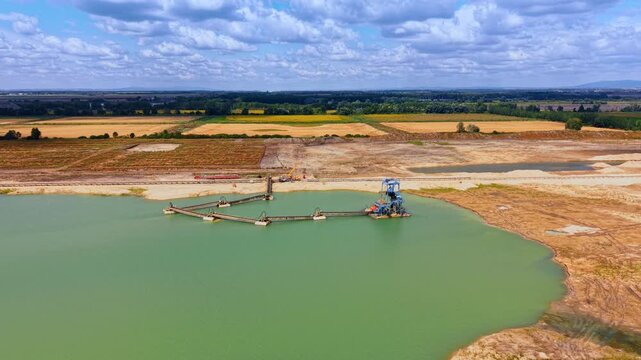 Quarry dredging installation beside excavated banks. Linked platforms extend across green water toward a blue tower, with earthworks and farmland behind.