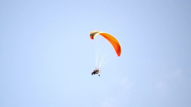 Parachutist soars through clear blue sky. Orange wing glides with quiet grace. Adrenaline hums in every graceful turn. Perfect for adventure, freedom, or travel themes