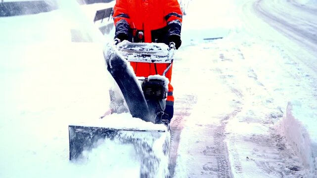 Snow clears with powerful machine. Worker in bright gear pushes snowblower steadily. Snow sprays as road clears for safe travel. Ideal for winter maintenance or seasonal campaigns