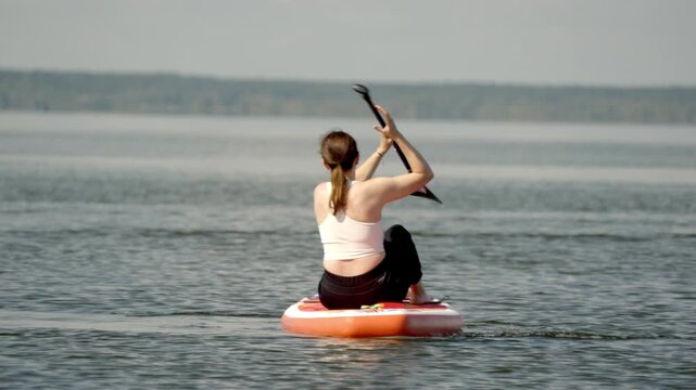 Woman paddles calm lake on inflatable board. She moves smoothly through gentle waters. Her focus suggests enjoyment and peace. Perfect for outdoor recreation or fitness themes