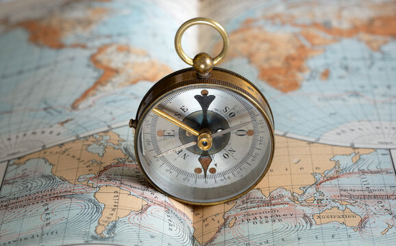 Vintage brass compass on an old geographic map close up. Antique navigation instrument for travel, exploration, geography and discovery concept. Adventure, tourism, cartography and orientation theme.