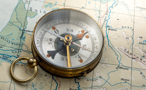 Vintage brass compass on an old geographic map close up. Antique navigation instrument for travel, exploration, geography and discovery concept. Adventure, tourism, cartography and orientation theme.