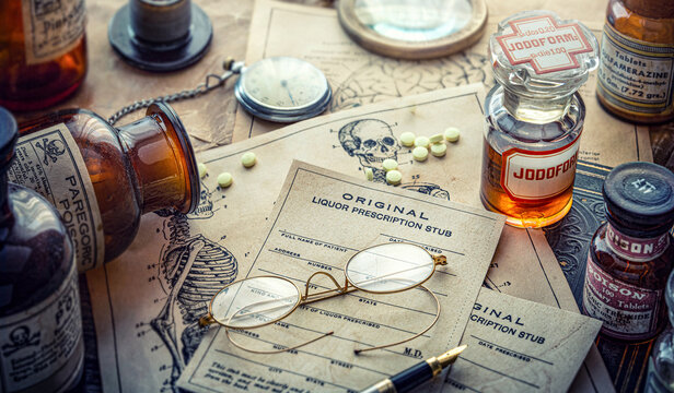 Old medical medicines in bottles, medical prescriptions, glasses and a pen on the table in the doctor's office. Old medical, pharmaceutical and scientific background.