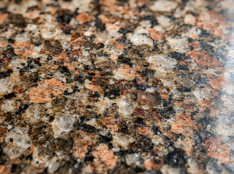 Macro view of polished granite stone slab showing intricate pattern of mineral grains in shades of brown orange and black transparent