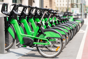 Obraz premium A row of green electric bicycles parked at an urban public bikeshare docking station on a city street.