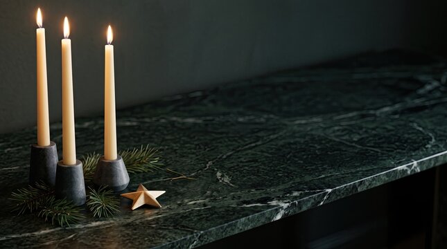 Three lit taper candles in concrete holders with a small gold star and pine branches on a dark green marble surface with copy space