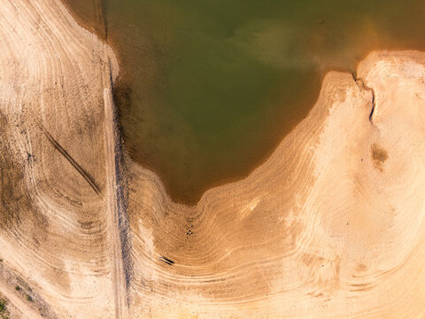 An aerial view of a drying reservoir with receded water levels exposing arid, cracked soil due to extreme drought and climate change