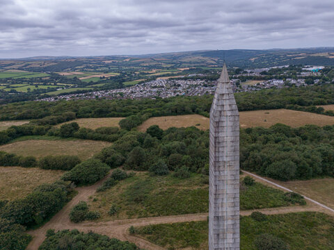 Aerial view of the stone Bodmin Monument rising above the surrounding fields and trees with the town of Bodmin in the background in Bodmin, Cornwall, United Kingdom.