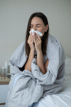Sick woman resting in bed with symptoms of fever, runny nose and cough during an illness