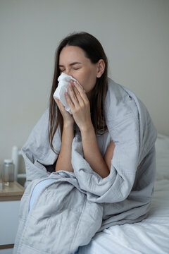 Sick woman resting in bed with symptoms of fever, runny nose and cough during an illness