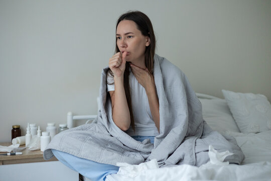 Sick woman resting in bed with symptoms of fever, runny nose and cough during an illness