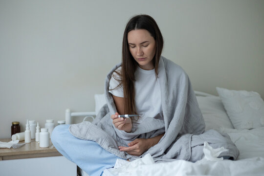 Sick woman resting in bed with symptoms of fever, runny nose and cough during an illness