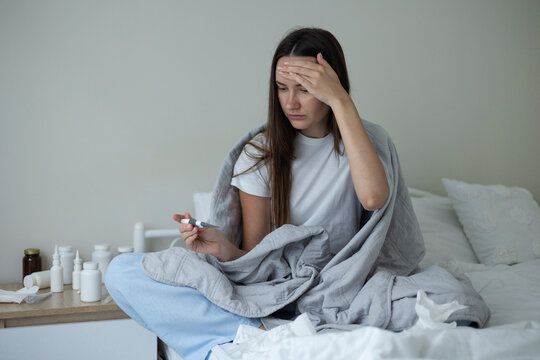 Sick woman resting in bed with symptoms of fever, runny nose and cough during an illness