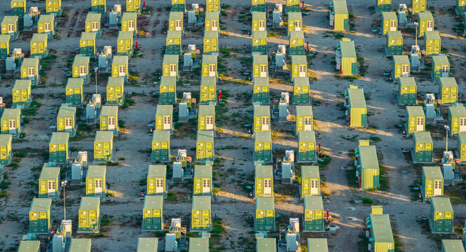 Aerial view of a large battery energy storage facility with modular container units arranged in repetitive rows across a gravel field in the industrial landscape. Trino, Piedmont, Italy.