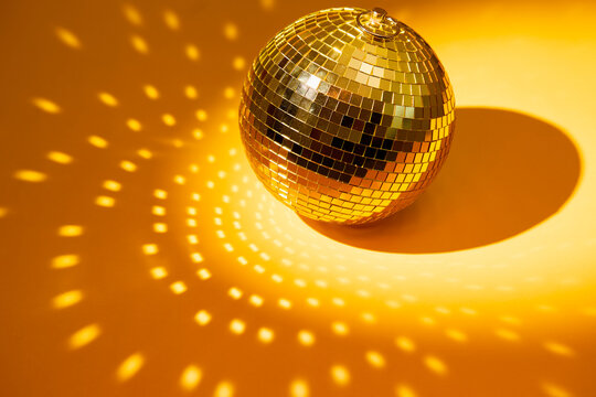 Gold disco mirror ball on a yellow surface with scattered light reflections.