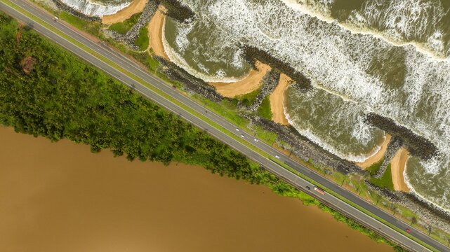 Aerial view of Maravanthe beach showing the narrow land strip between the Arabian Sea and Souparnika River with a coastal road running parallel to the shore in Maravanthe, Karnataka, India.