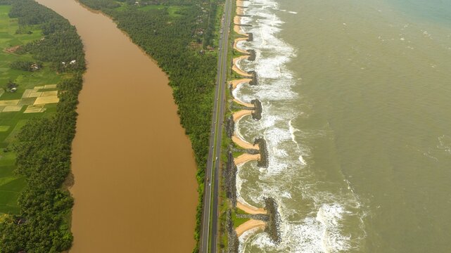 Aerial view of Maravanthe beach featuring the Arabian Sea on one side and the Souparnika River on the other, separated by a coastal highway in Maravanthe, Karnataka, India.