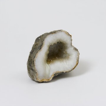 A geode with a white crystalline interior is showcased against a neutral background